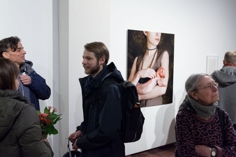 Visitors are chatting. In the background hangs a photo of a woman carrying a skinned rabbit in her arms.