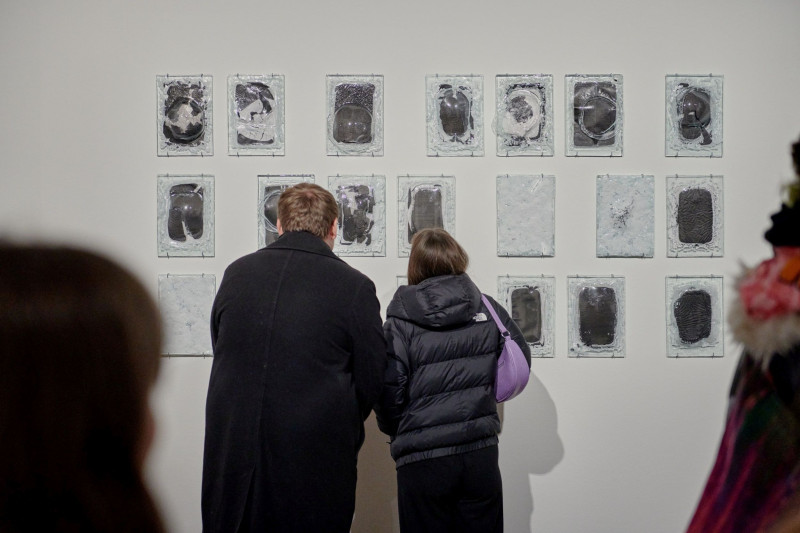 A man and a woman are looking at glass works that are attached to the wall in several rows