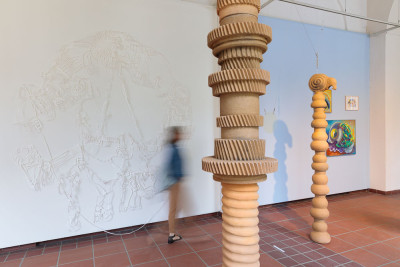 Artworks in the form of ceramic columns in the foreground and a paper cut in the background on the wall, with a person standing between them