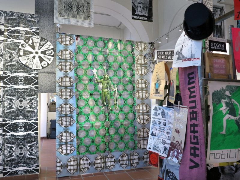 Vielzahl verschiedenformatiger Drucke und Gegestände hängend im Raum verteilt.