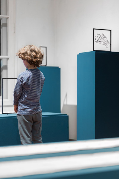 A child stands in front of a low pedestal. Next to him is a high pedestal on which a work of art in the shape of a hand is placed