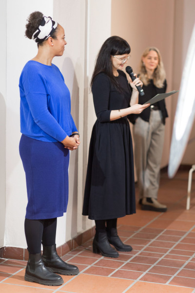 Three women. The woman in the middle is the curator speaking into a microphone