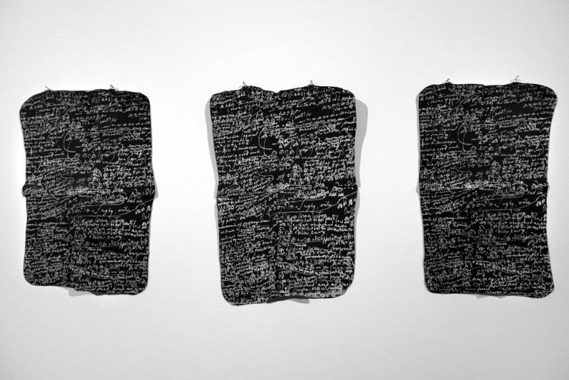 Drei schwarze Rechtecke mit weißen Schriftzeichen sind auf einer weißen Wand angebracht.