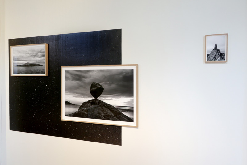 Three different-sized black-and-white photographs each show balancing blocks of stone in different natural landscapes. Behind them is a section of the universe on a photo wallpaper.