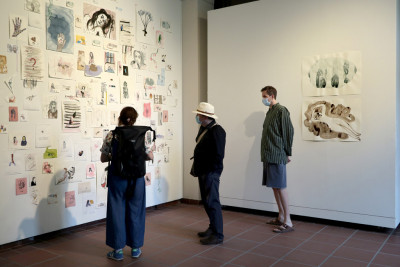 Three visitors stand in front of two walls which a multitude of drawings hang.