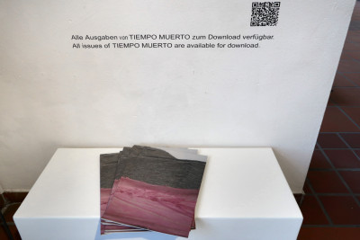 A few copies of the magazine TIEMPO MUERTO (Dead Time) are lying on a bench for viewers to look at