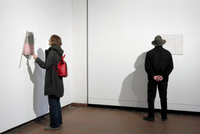 Two people in the exhibition room. A woman is flipping through the magazine TIEMPO MUERTO (Dead Time), which is mounted on the wall for viewing. A man stands in front of an excerpt from the magazine, which is attached to the wall as a single sheet