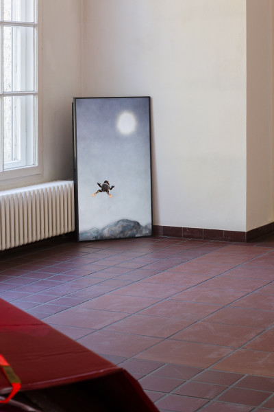 Monitor leaning against a wall showing a video still which depicts a frog jumping through a moonlit sky above a mountain landscape.