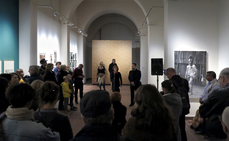 Raumansicht. Die Besucher haben sich versammelt um sich die Eröffnungsrede anzuhören.