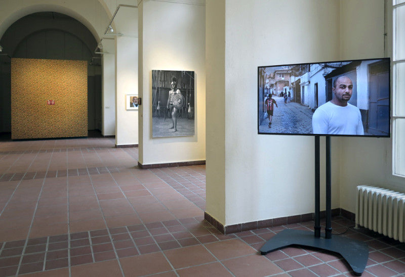 Exhibition view. A screen with a photo on it in the foreground. More photos on the walls behind it.