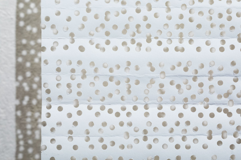 Cut-out of white sheet of paper with countless holes.