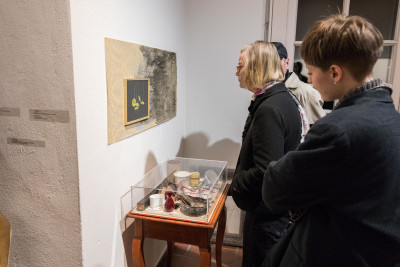 Besucherinnen betrachten eine Blumenzeichnung, deren Rahmen auf einer Tapete befestigt ist. Darunter steht ein kleiner Tisch mit unterschiedlichen Gegenständen.