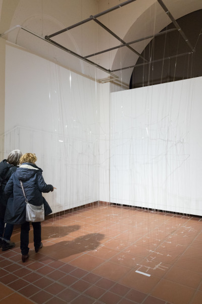 Den Galerieraum nimmt eine überlebensgroße Struktur aus durchsichtigen Klebestreifen ein. Zwei Betrachtende stehen davor.