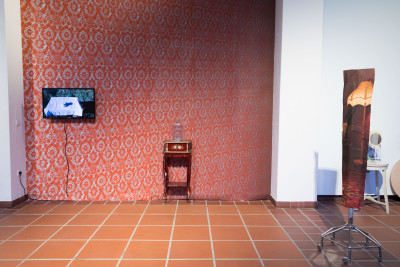 On the wall is red patterned wallpaper, a TV and  a small table with a glass bonnet. with a glass bonnet.