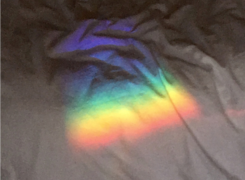 Auf dem Bild ist ein Regenbogen auf einer weißen Bettdecke zu sehen.