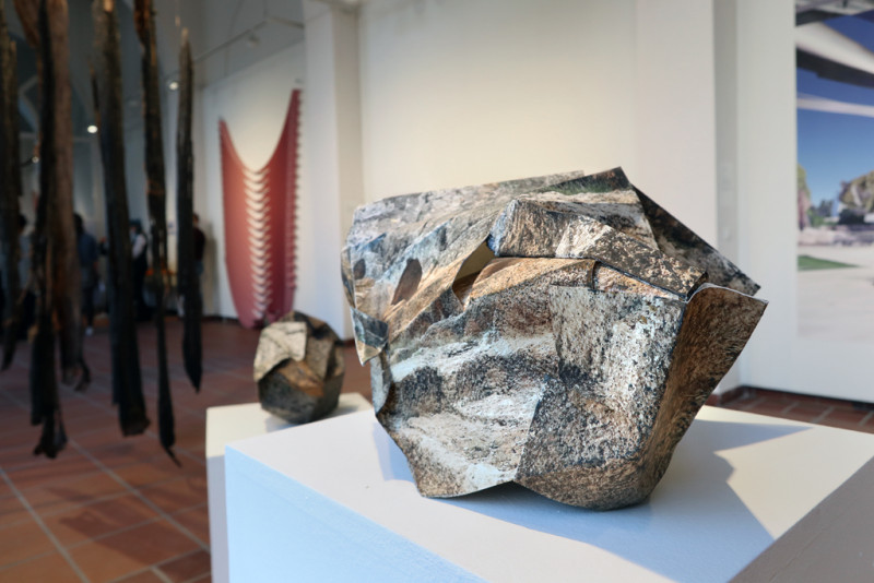 Nahaufnahme eines Papierobjekts, das einen Stein imitiert. Im Hintergrund weitere Werke der Ausstellung.