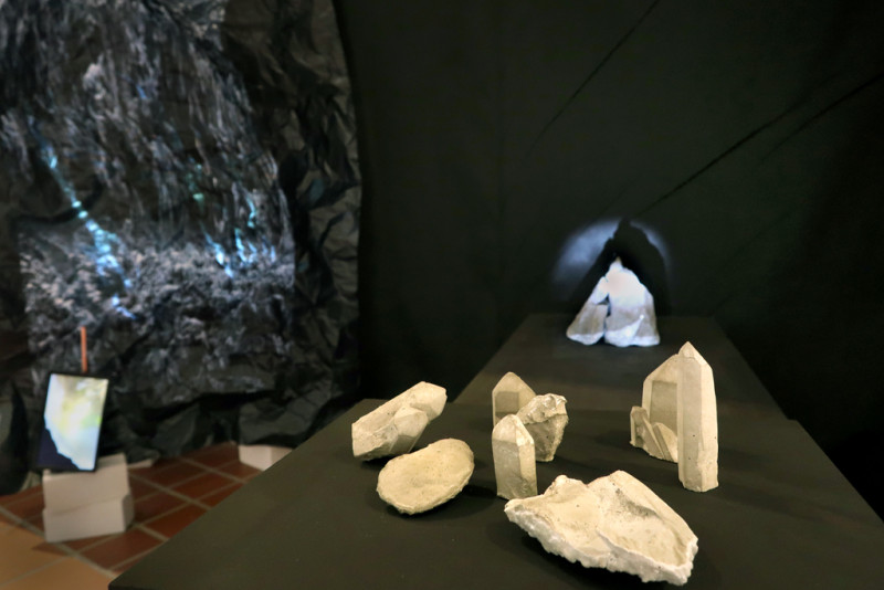 Auf einem schwarzen Tisch befinden sich im Vordergrund Betonkritsalle, dahinter eine schwraze Wand mit dem Bild eines Gletschers.