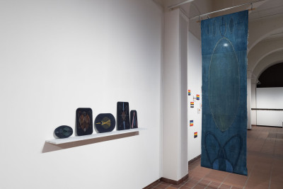 Dark embroidered  plates stand  on a board on the wall. Next to it hangs a blue cloth.