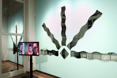 Room installation. Curved mirrors hang radially on the wall. In front of it is a screen.