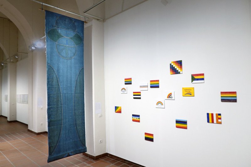 Bilder mit bunten Streifen hängen an der Wand, ein blaues Tuch daneben.