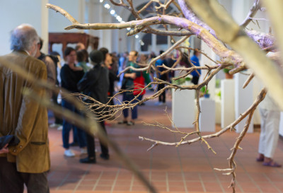 Branches without leaves and behind them a crowd in the gallery space