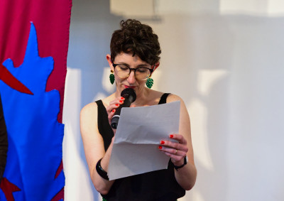 Female curator speaks into a microphone while looking down at papers she is holding in her hand