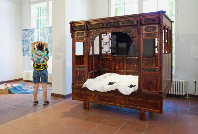 Box-shaped bed made of solid wood with a decorative roof and elaborate carvings, including figurative depictions and Chinese characters