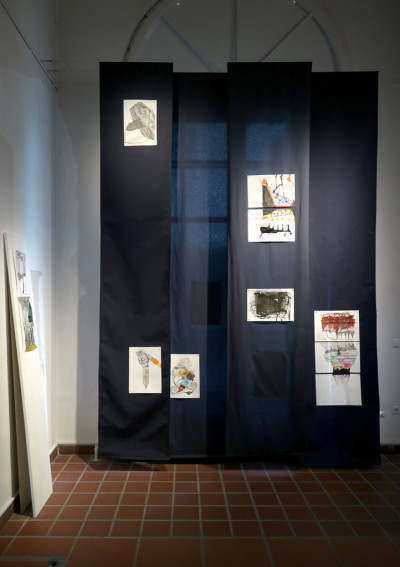 Nine drawings in ink and felt-tip pen are attached to a floor-length dark blue curtain.