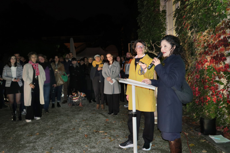 Eine Gruppe von Menschen steht versammelt um eine Rednerin, die ein Mikrofon in der Hand hält.