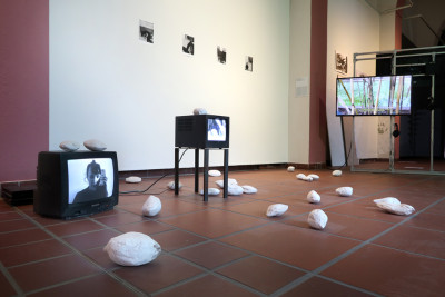 View of the exhibition featuring two works that include screens, photographs, and elongated round plaster molds scattered on the floor and some screens.