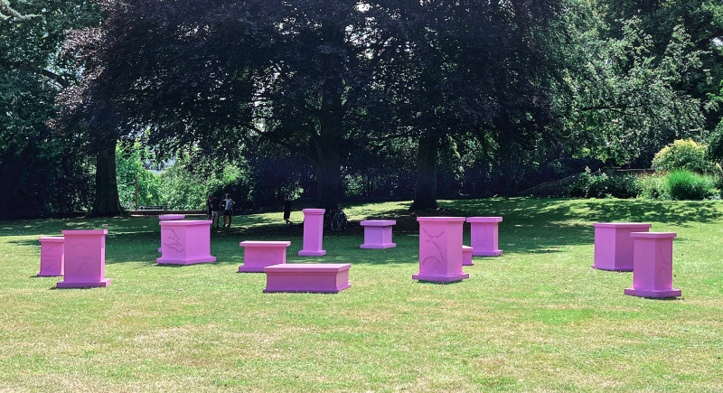 Different sized pedestals in pink color stand on a meadow
