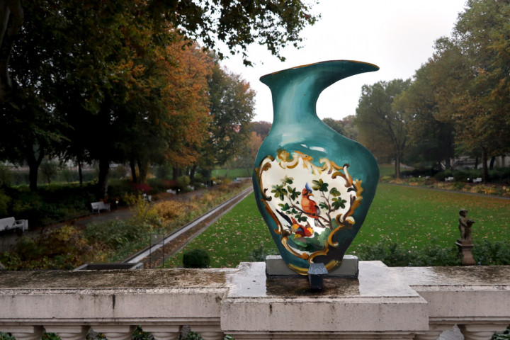 Eine Vase aus Pappe in grünem Ton und einem Vogelmotiv auf der Balustrade mit Blick in den Körnerpark im Hintergrund