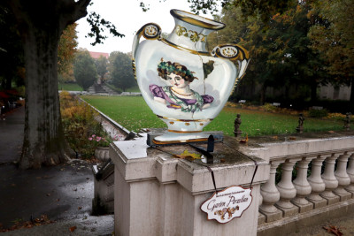 Eine weiße Vase aus Pappe mit dem Portrait eines römischen Kaisers auf der Ecke der Balustrade, dadrunter hängt ein Schild mit der Aufschrift 