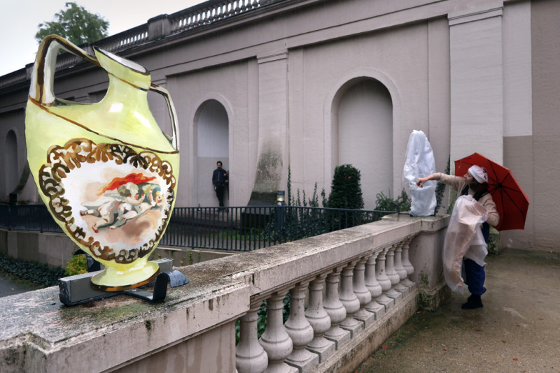 Im Vordergrund eine Blumenvase auf der Balustrade und im Hintergrund die Künstlerin beim Entpacken einer weiteren Arbeit