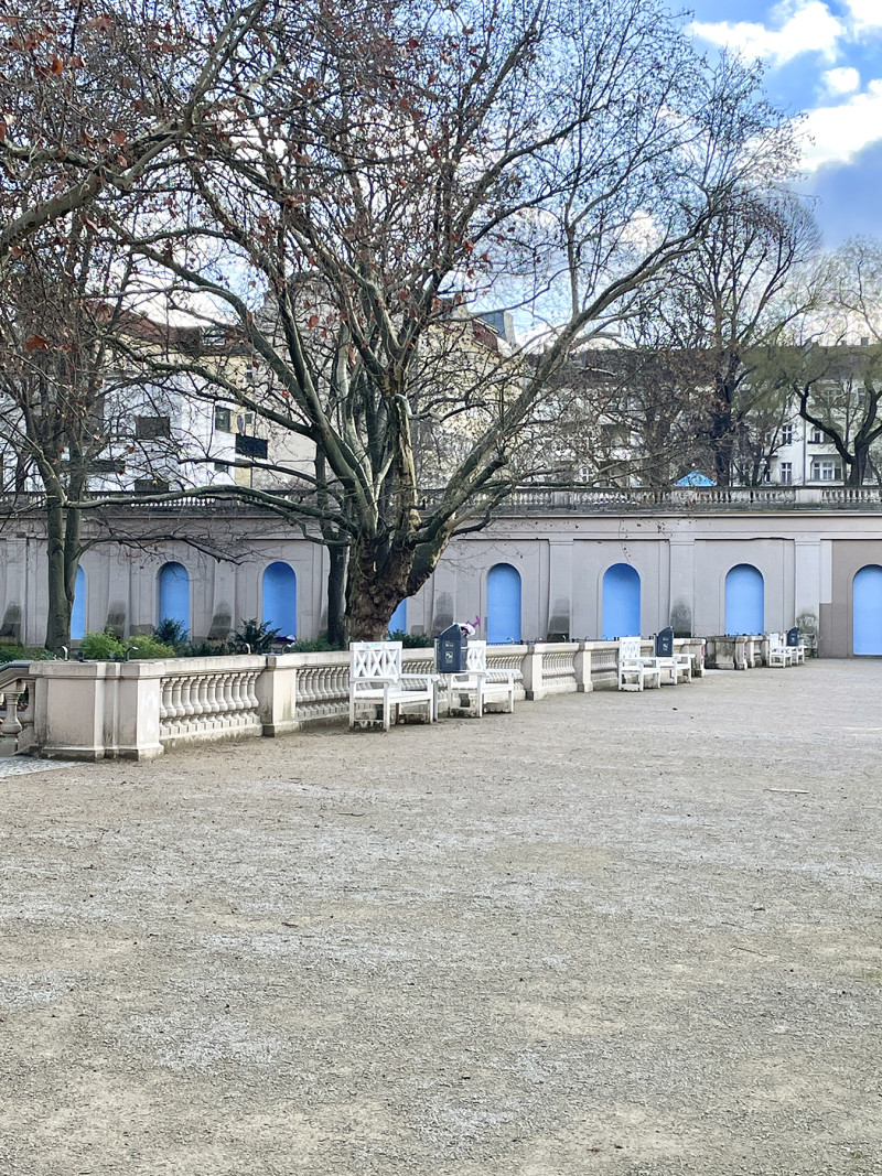 In Körnerpark, blue posters are displayed in the arcades of the wall. Körnerpark sind blaue Plakate in den Arkaden der Wand plakatiert.