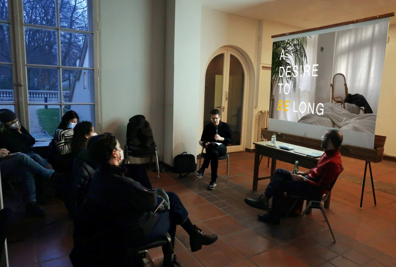 Präsentation des Künstlers Omar Kasmani auf der Leinwand. Im Vordergrund sitzen Künstler Osmar Kasmani und der Prof. Hansjörg Dilger (FU Berlin))