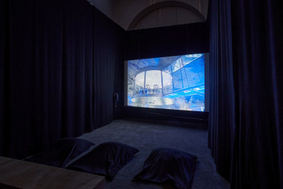 Ein dunkler Screeningroom, im Vordergrund Sitzkissen auf dem Boden, am Kopfende läuft ein Video.