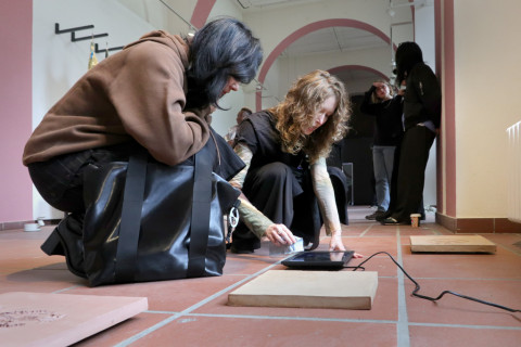 The artists are bent over a work of art in the exhibition.