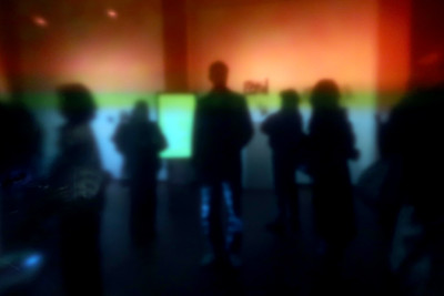 Man sieht Menschen in einer Ausstellung durch eine farbige Glasscheibe. Das Bild ist dadurch verschwommen.