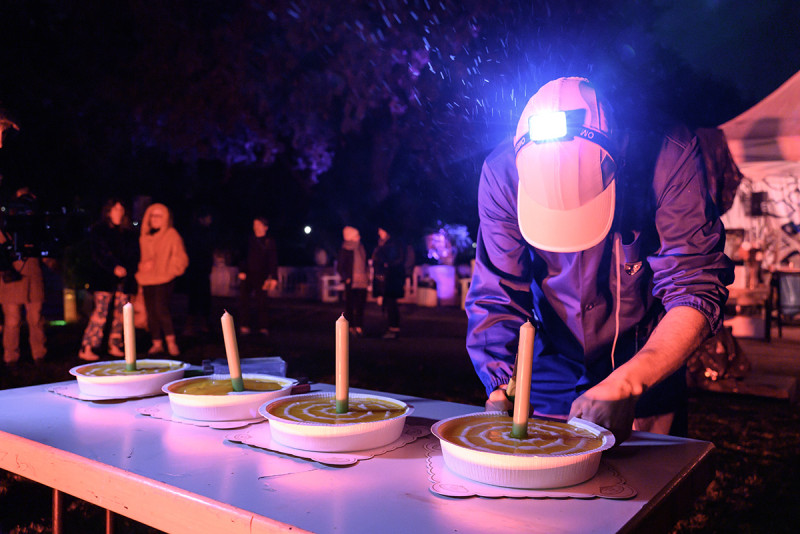 Lalo Gomes von dem Kollektiv LaLoVe’s Kitchen serviert den Geburtstagskuchen mit hell leuchtender Kopflampe im Bildvordergrund