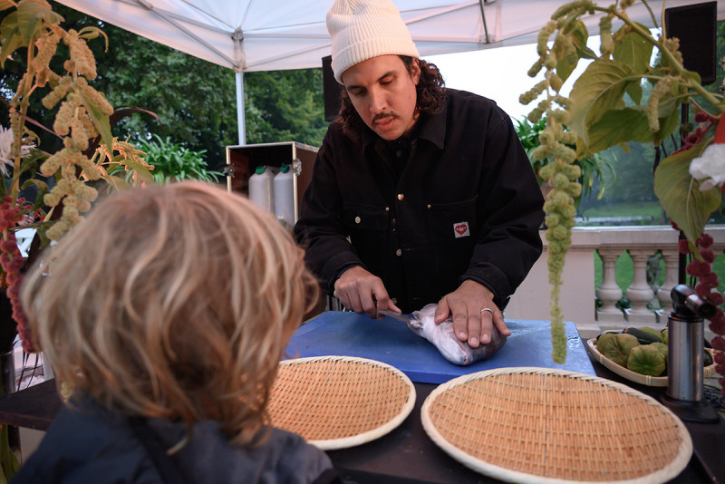 Dauwd Al Hilali vom Kollektiv African Acid is the Future filetiert einen Fisch und ein Kind beobachtet dieses Szenario