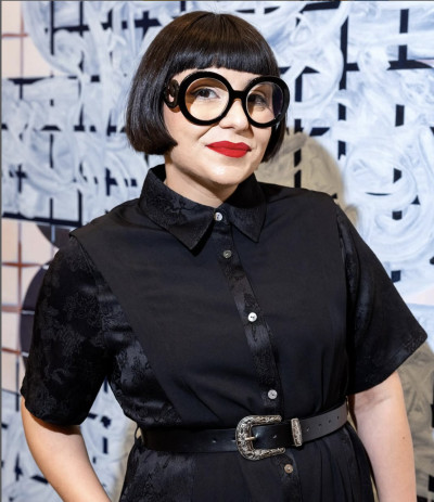 Frau mit schwarzer Bob-Frisur, runder Brille und schwarzem Kleid mit Gürtel