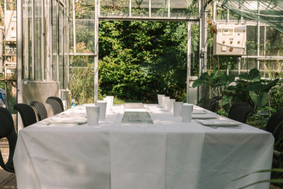 Gedeckter Tisch in einem Gewächshaus für eine Dinner-Performance mit Blick auf begrünte Außenflächen