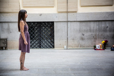 Eine Frau steht links im Bild - rechts liegen Blumben der Trauer an die Hauswand gelehnt